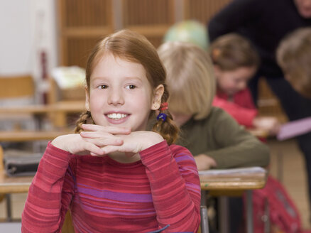 Mädchen (4-7) im Klassenzimmer, lächelnd, Kopf auf Händen, Nahaufnahme - WESTF04575