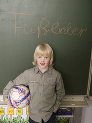 Boy (4-7) standing in front of blackboard, holding football, portrait - WESTF04568