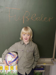 Junge (4-7) vor einer Tafel stehend, mit Fußball in der Hand, Porträt - WESTF04568