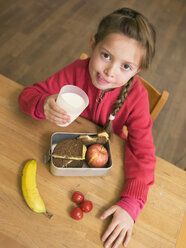 Mädchen (4-7) hält ein Glas Milch und eine Brotdose am Schreibtisch, Blick von oben - WESTF04548