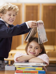 Kinder (4-7) im Klassenzimmer, Junge hält Buch über den Kopf des Mädchens, lächelnd - WESTF04541