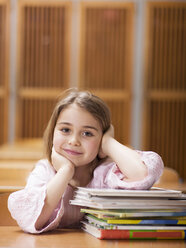 Girl (4-7) sitting desk, leaning on stack of books, smiling, portrait - WESTF04539