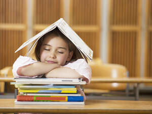 Mädchen (4-7) am Schreibtisch sitzend, auf einen Bücherstapel gestützt, Augen geschlossen - WESTF04538