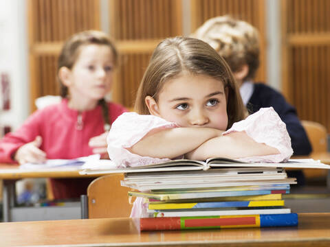 Mädchen (4-7) am Schreibtisch sitzend, auf einen Bücherstapel gestützt, lizenzfreies Stockfoto