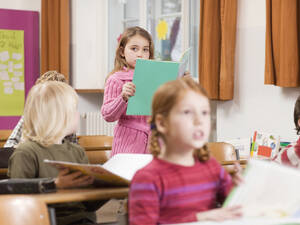 Kinder (4-7) im Klassenzimmer, Fokus auf Mädchen, das im Hintergrund ein Buch liest - WESTF04534