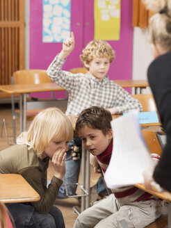 Junge (4-7) hebt Hand im Klassenzimmer, Fokus auf flüsternde Jungen im Vordergrund - WESTF04500