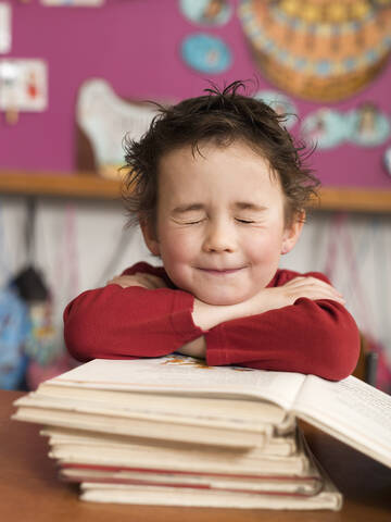 Junge (4-5) am Schreibtisch sitzend und auf einen Bücherstapel gestützt, Augen geschlossen, Nahaufnahme, lizenzfreies Stockfoto