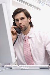 Businessman sitting by computer, using landline phone, close-up - WESTF04848