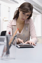 Junge Frau benutzt einen Taschenrechner im Büro - WESTF04773