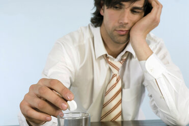 Businessman holding pill, sitting on desk with glass of water, close-up - WESTF04768