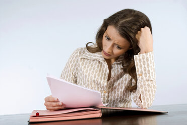 Young woman reading document scratching head - WESTF04732