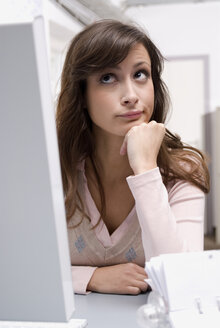 Junge Frau sitzt im Büro am Computer und schaut nach oben, Nahaufnahme - WESTF04725