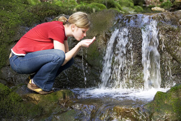 Junge Frau trinkt Wasser aus einem Bach, Seitenansicht - WWF00280