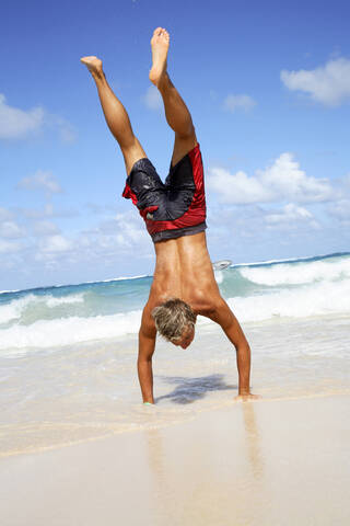 Junger Mann macht Handstand am Strand, lizenzfreies Stockfoto