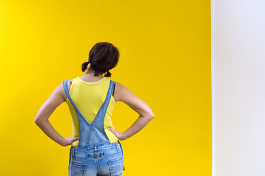 Woman standing in front of yellow wall, rear view - HHF01273