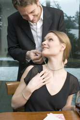 Mann befestigt Halskette am Hals einer Frau - NHF00523