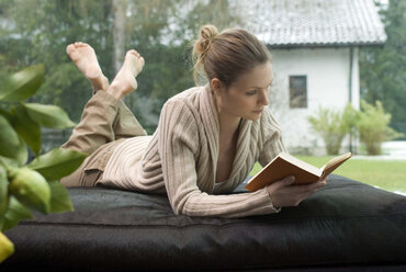 Junge Frau entspannt sich auf dem Sofa und liest ein Buch - NHF00436