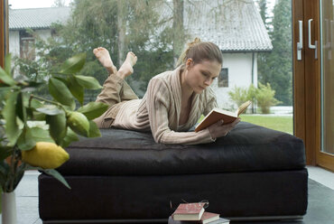 Junge Frau entspannt sich auf dem Sofa und liest ein Buch - NHF00435