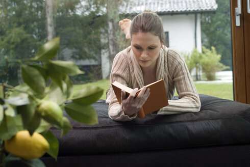 Junge Frau entspannt sich auf dem Sofa und liest ein Buch - NHF00434