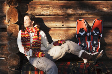Frau mit Schneeschuhen vor einer Hütte sitzend - HHF01361