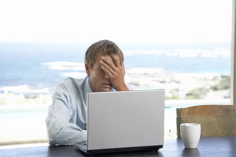 Mann sitzt am Tisch und benutzt einen Laptop, lizenzfreies Stockfoto