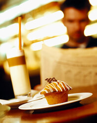 Muffin auf Teller, Person hält Papier im Hintergrund - CHKF00441