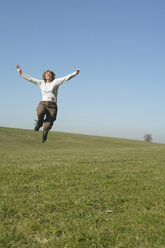Frau springt auf einer Wiese, Arme hoch - GNF00916