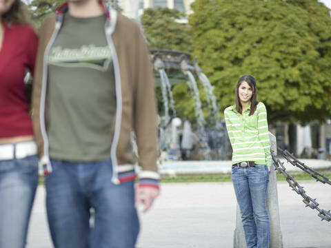 Junge Frau lehnt sich an einen Pfahl und beobachtet ein Paar, lizenzfreies Stockfoto