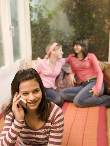 Mädchen (16-17) telefoniert, Freundinnen sitzen im Hintergrund, lizenzfreies Stockfoto