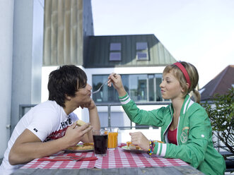 Young woman feeding young man on balcony - KMF00897