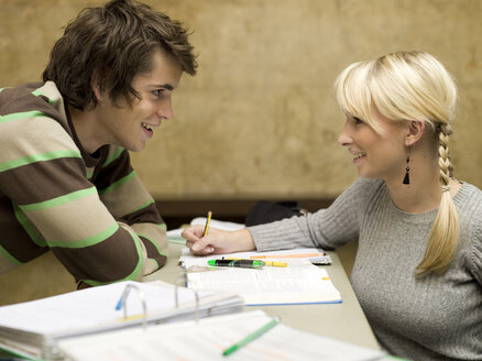 Young woman sitting on desk, looking at young man - KMF00876