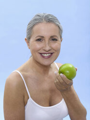 Woman holding green apple, portrait - WESTF05307