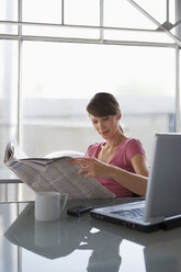 Woman at desk reading newspaper - WESTF05591