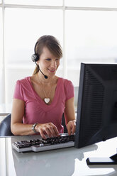 Frau arbeitet am Computer und trägt ein Headset - WESTF05546