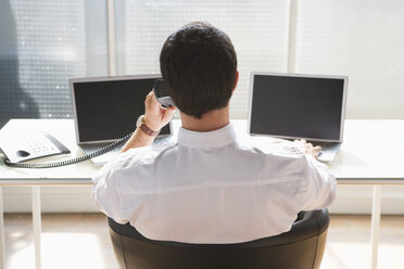 Geschäftsmann beim Telefonieren, zwei Laptops auf dem Schreibtisch, Rückenansicht - WESTF05524