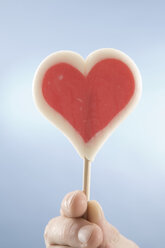 Hand hoding heart-shaped lollipop, close-up - CLF00437