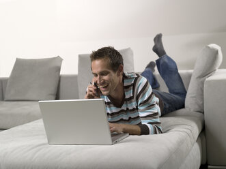 Mann auf dem Sofa liegend, mit Laptop und Mobiltelefon - WESTF05987