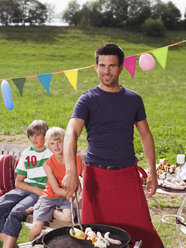 Father preparing barbecue, children in background - WESTF06064