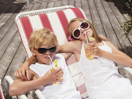 Brother and sister lying in deck chairs, drinking juice - WESTF06012