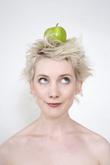 Junge Frau, die einen Apfel auf dem Kopf balanciert, Porträt - TCF00196