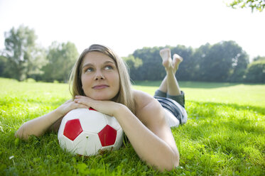 Woman (20-25) lying in field, leaning on football, close-up - CKF00160