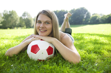 Woman (20-25) lying in field, leaning on football, close-up - CKF00159