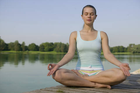 Frau (20-25) übt Yoga auf dem Steg, lizenzfreies Stockfoto