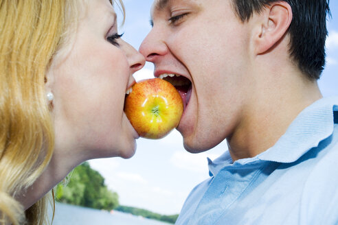 Porträt eines jungen Paares, das in einen Apfel zwischen ihren Mündern beißt - SEF00013