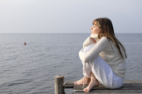 Italien, Gardasee, Junge Frau (20-25) sitzt auf Steg - DKF00131