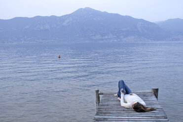 Italy, Lake Garda, Young woman (20-25) lying on jetty - DKF00126