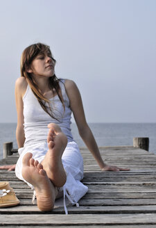 Italy, Lake Garda, Young woman (20-25) sitting on jetty, close-up - DKF00125