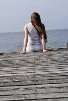 Italy, Lake Garda, Young woman (20-25) sitting on dock, rear view, close-up - DKF00118