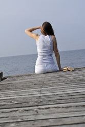 Italy, Lake Garda, Young woman (20-25) sitting on dock, rear view, close-up - DKF00117