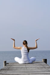 Italy, Lake Garda, Woman (20-25) exercising yoga on jetty - DKF00111